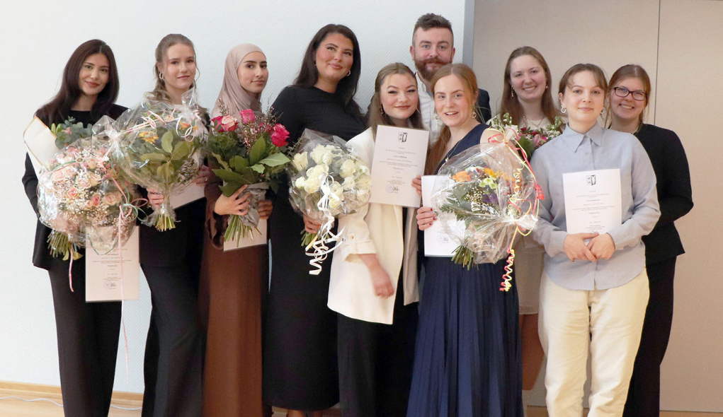 10 Azubis halten ihre Examenszeugnisse und Blumen in der Hand